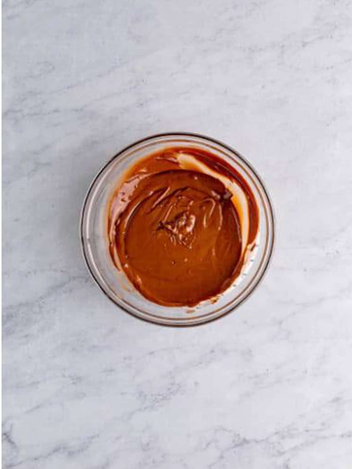 Smooth melted milk chocolate in a glass bowl.