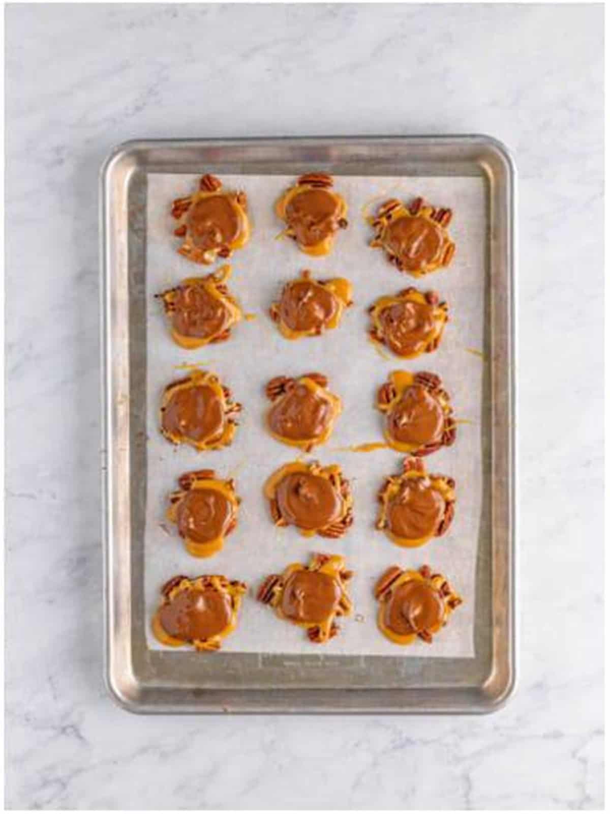 Finished turtle candies topped with melted chocolate on a tray.
