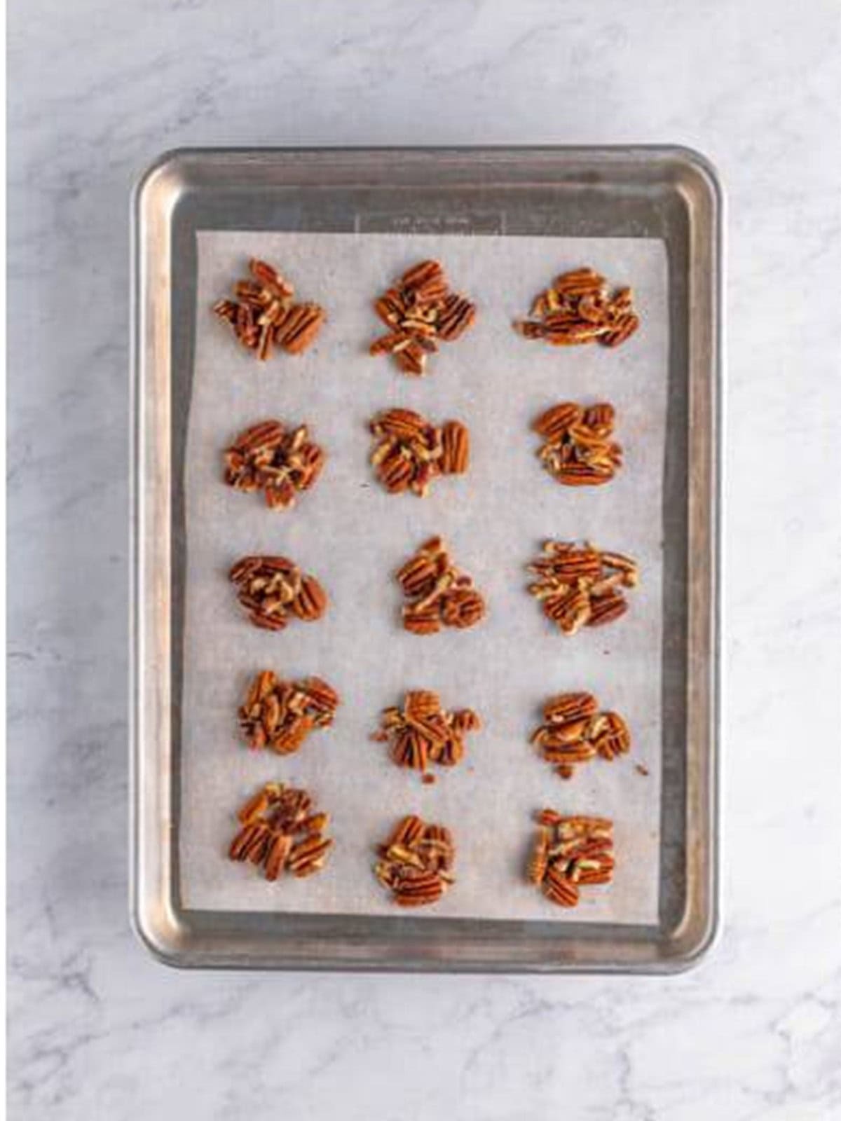 Pecan halves arranged in small piles on a parchment lined sheet tray.
