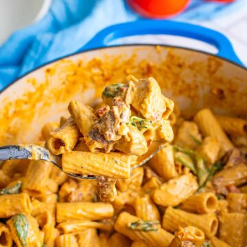 A pot of creamy Tuscan chicken pasta with rigatoni, spinach, and sundried tomatoes.
