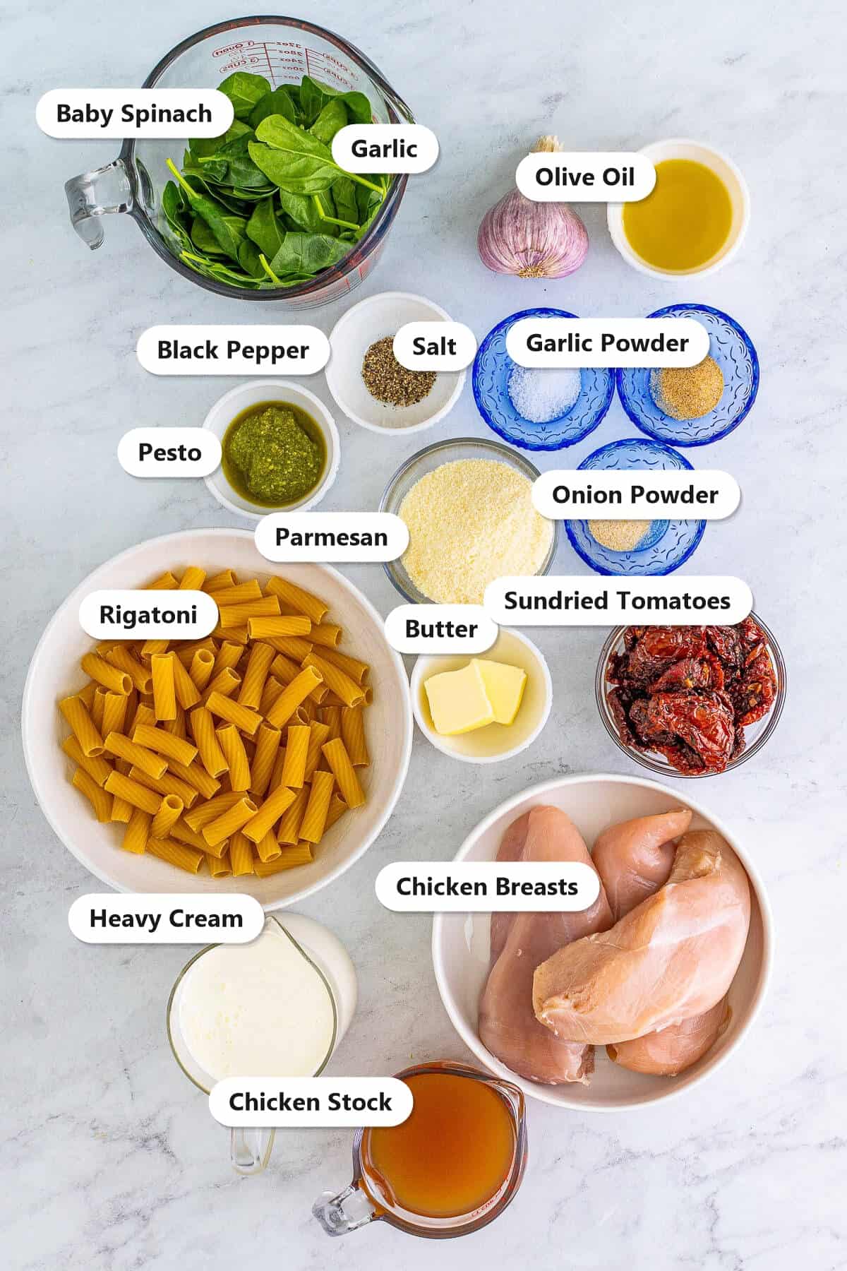 Labeled ingredients for Tuscan chicken pasta including chicken breasts, rigatoni, heavy cream, sundried tomatoes, baby spinach, parmesan, pesto, garlic, and seasonings.