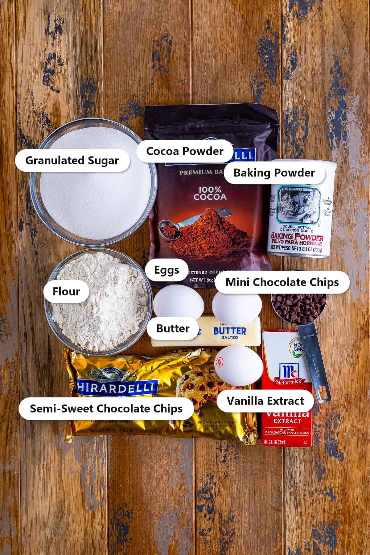 Labeled ingredients for two bite brownies including butter, semi-sweet chocolate chips, sugar, eggs, vanilla, flour, cocoa powder, baking powder, and mini chocolate chips.