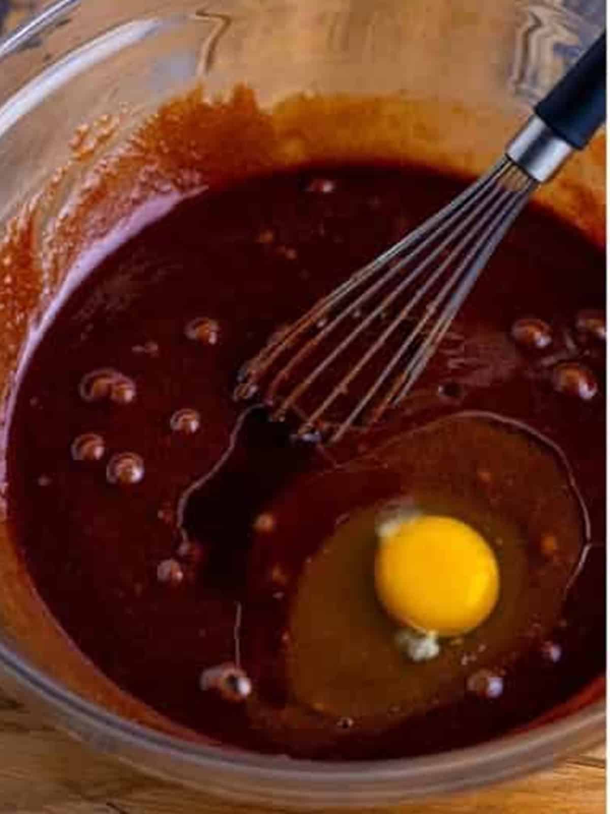 An egg being whisked into the melted chocolate and sugar for two bite brownies.