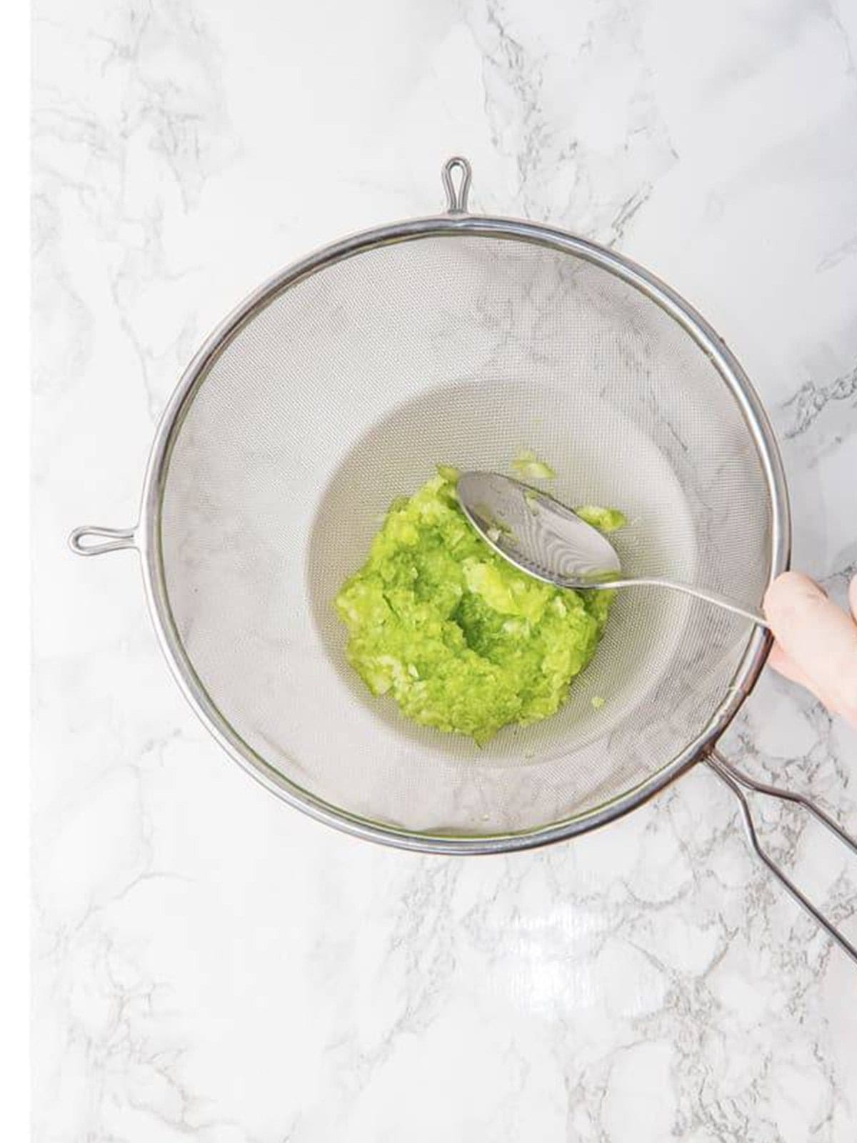 Squeezing the liquid out of grated cucumber in a strainer for tzatziki.