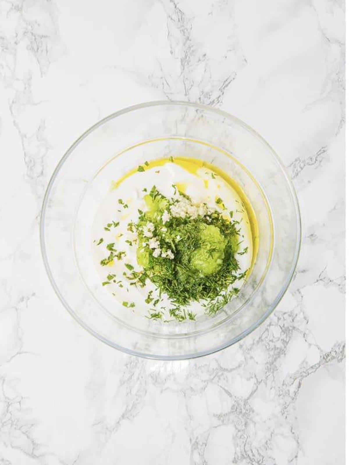 Stirring Greek yogurt with garlic, dill, lemon, and olive oil in a glass bowl for tzatziki.