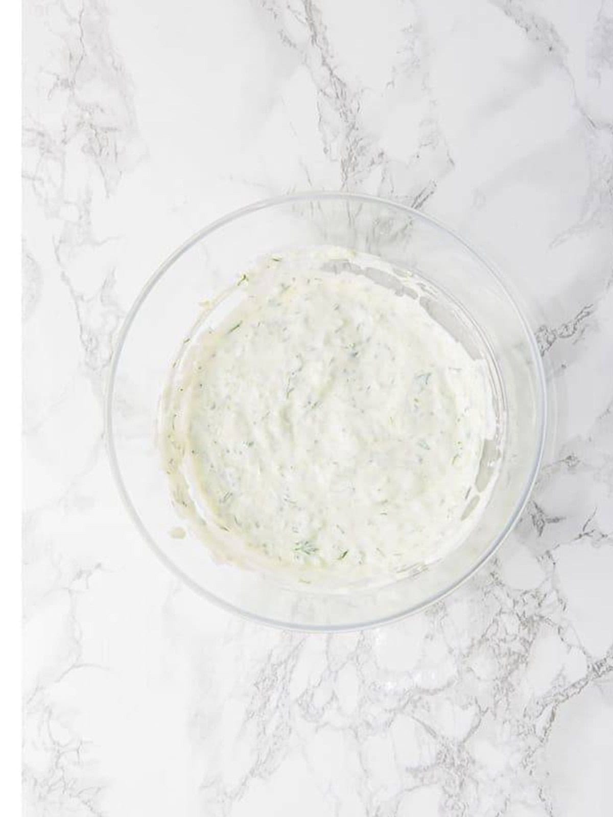 Finished creamy tzatziki sauce mixed in a glass bowl ready to chill.