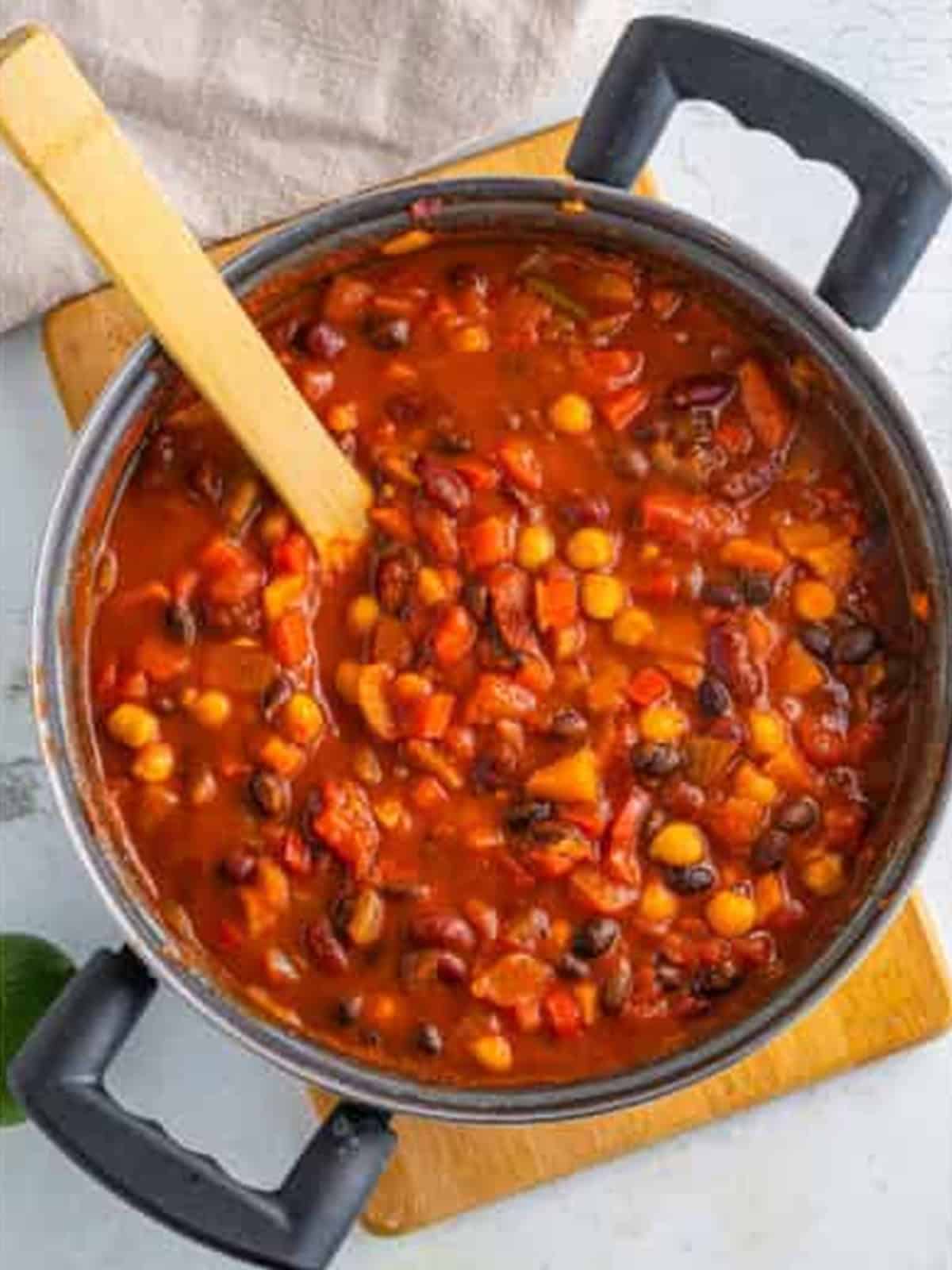Vegetarian chili simmering in a large pot with a wooden spoon.