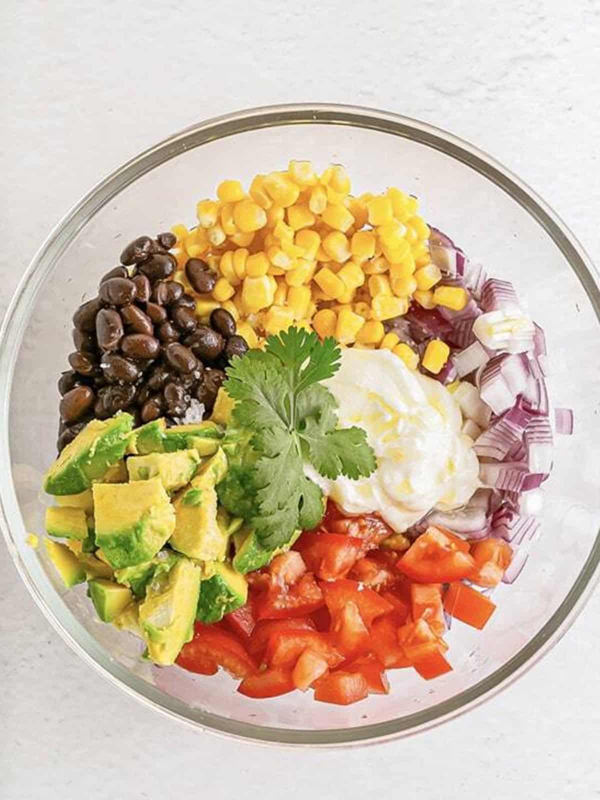 Adding black beans, corn, avocado, tomatoes, and seasonings to a bowl for vegetarian lettuce wraps.