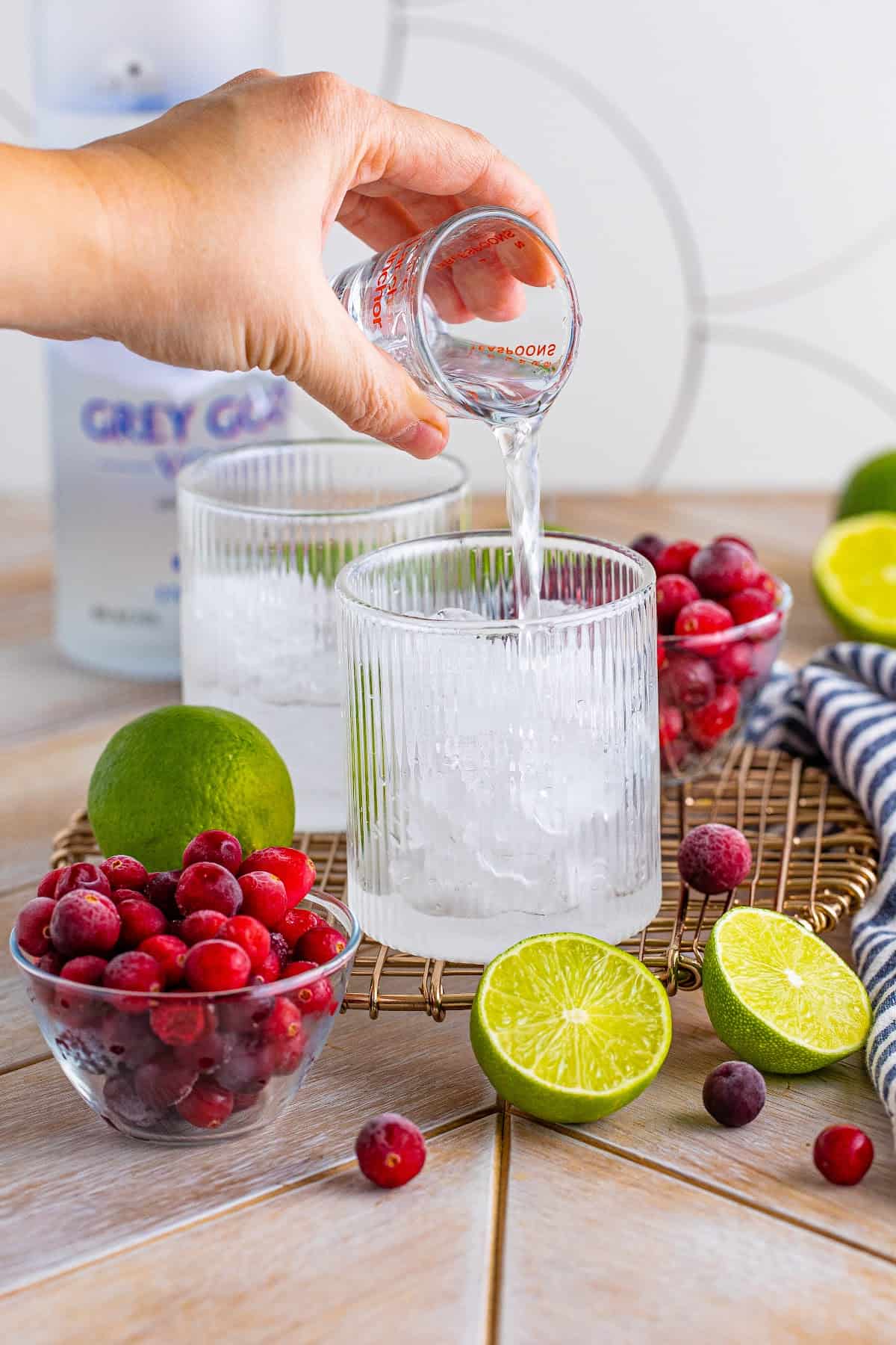 Pouring vodka over ice into a glass to make a Vodka Cranberry cocktail.