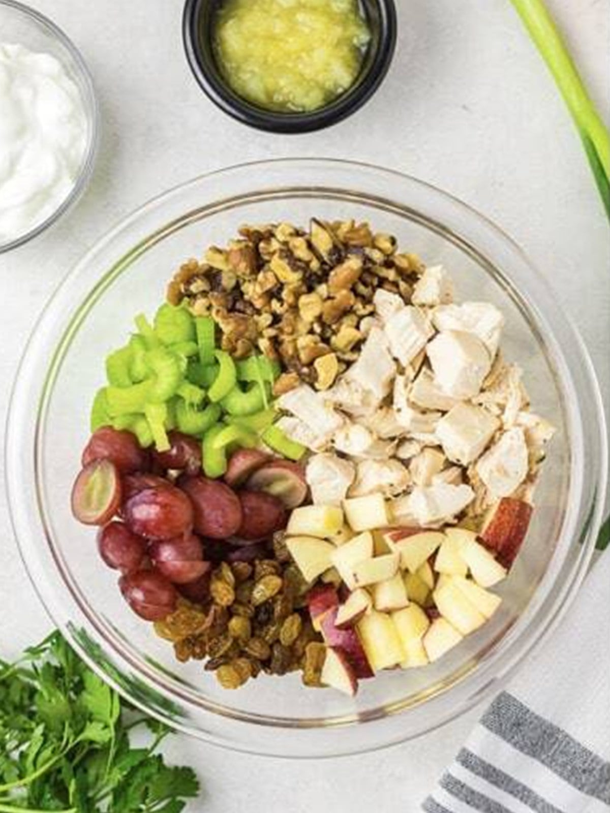 Chicken, apple, grapes, celery, walnuts, and raisins combined in a glass bowl.
