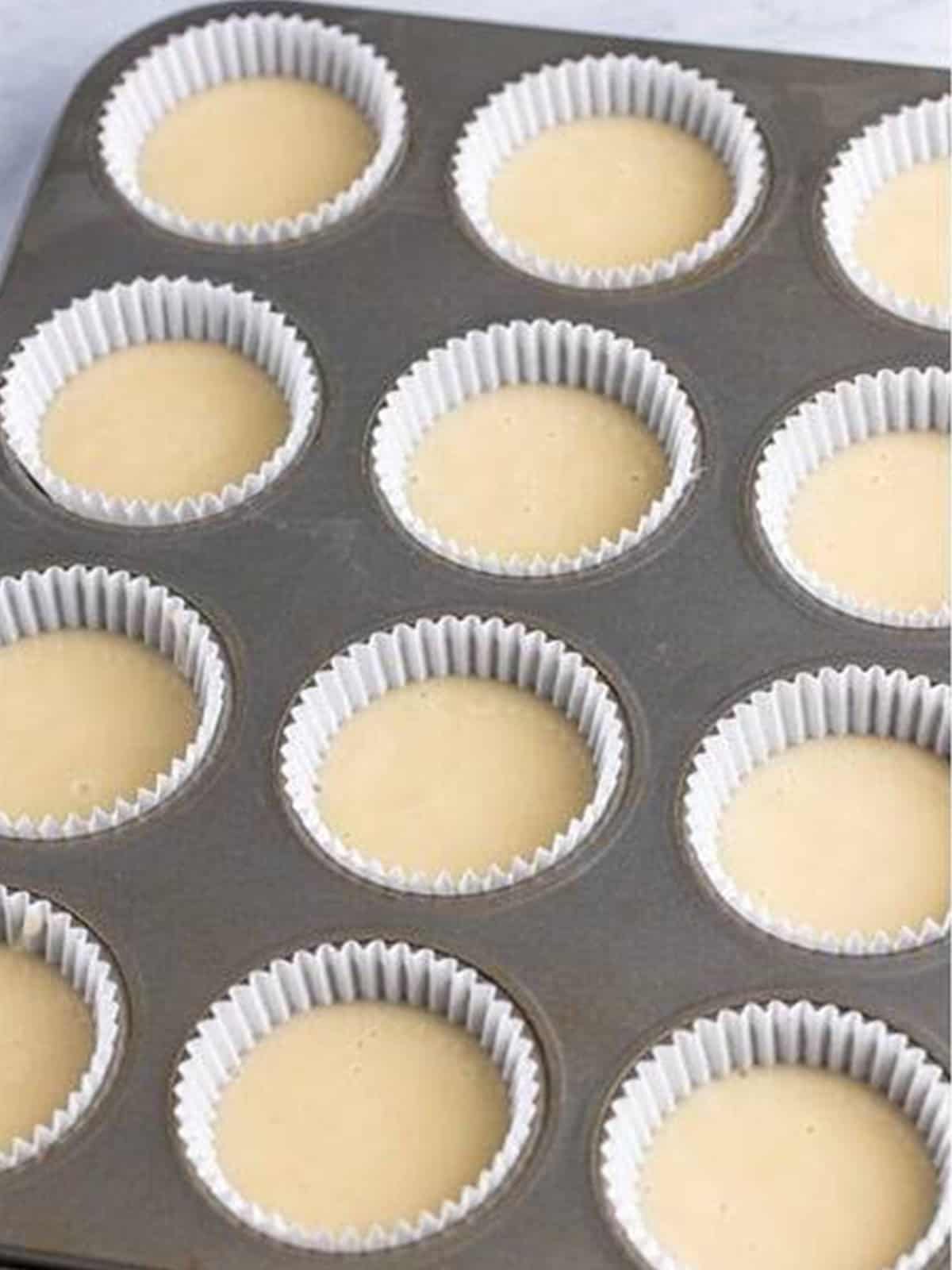 Cupcake liners filled with white wedding cake batter in a pan.
