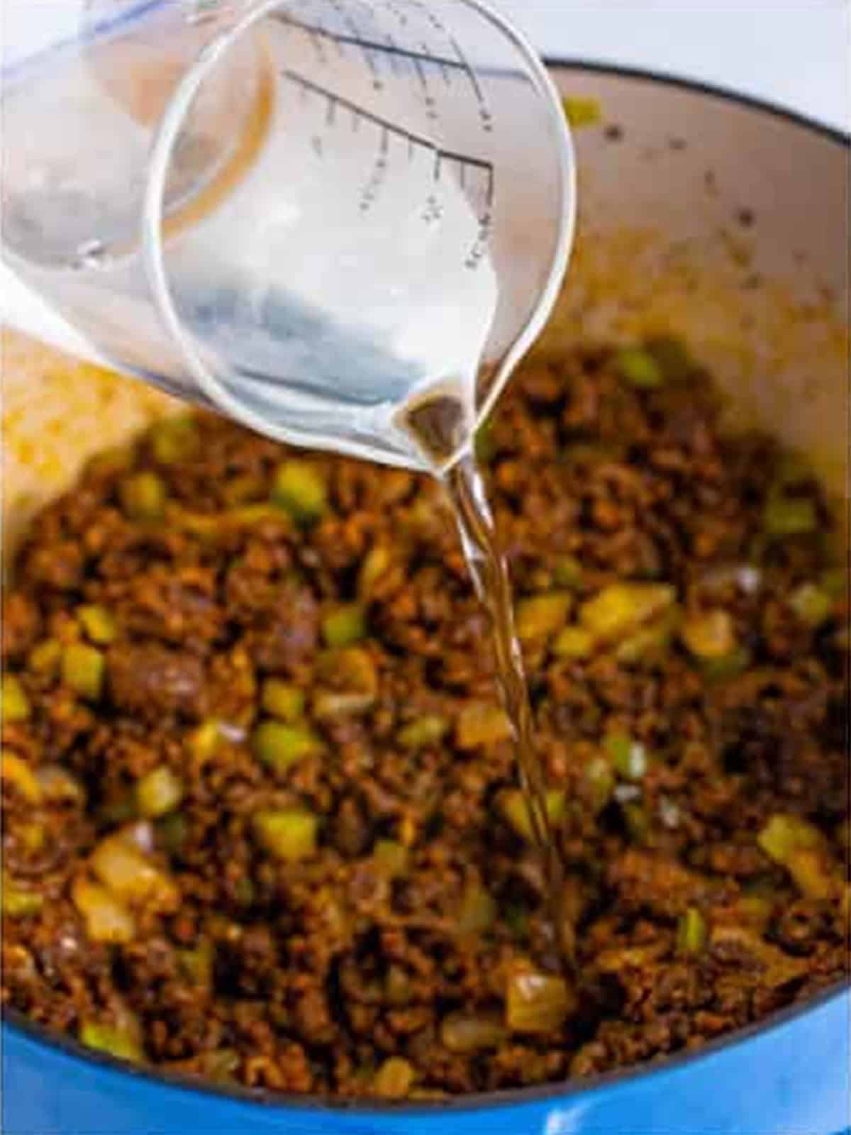 Water being poured into the pot of seasoned ground beef and vegetables.