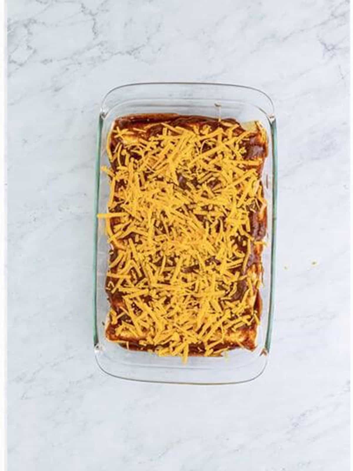 Red sauce and shredded cheddar spread over the rolled burritos.