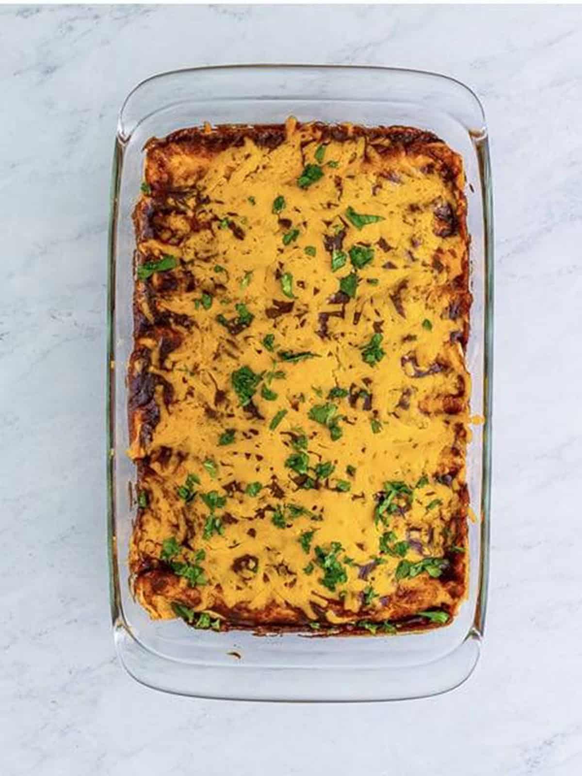 Baked wet burritos topped with melted cheese and fresh cilantro in the dish.