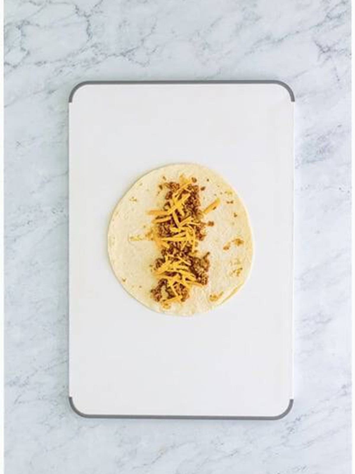 Ground beef filling spread down the center of a flour tortilla before rolling.