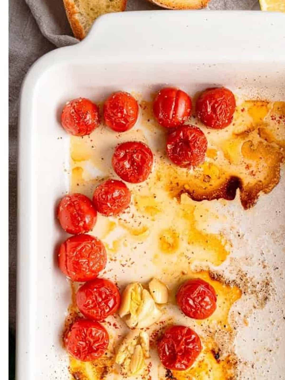 Roasted blistered cherry tomatoes and toasted crostini on a baking sheet.