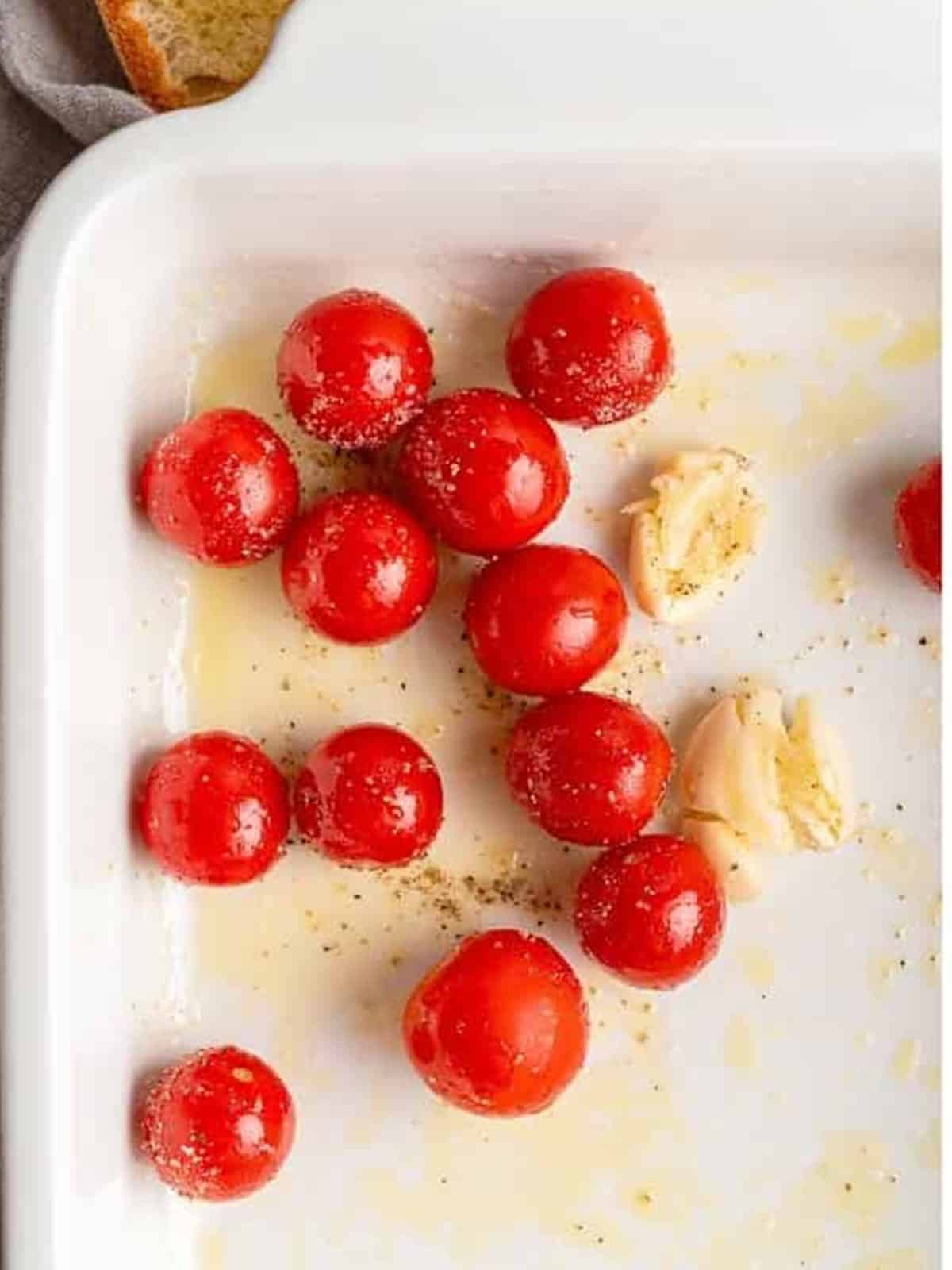 Cherry tomatoes and garlic tossed with olive oil in a baking dish for whipped ricotta dip.