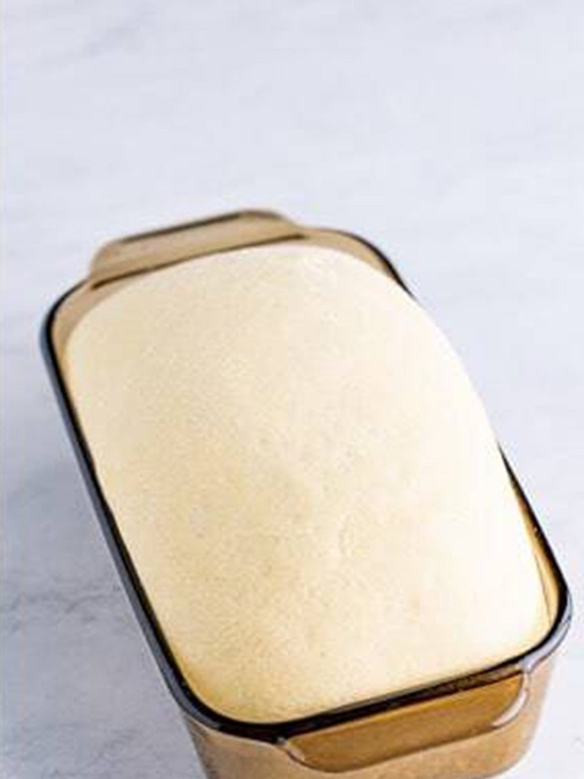 Shaped white bread dough rising in a loaf pan.