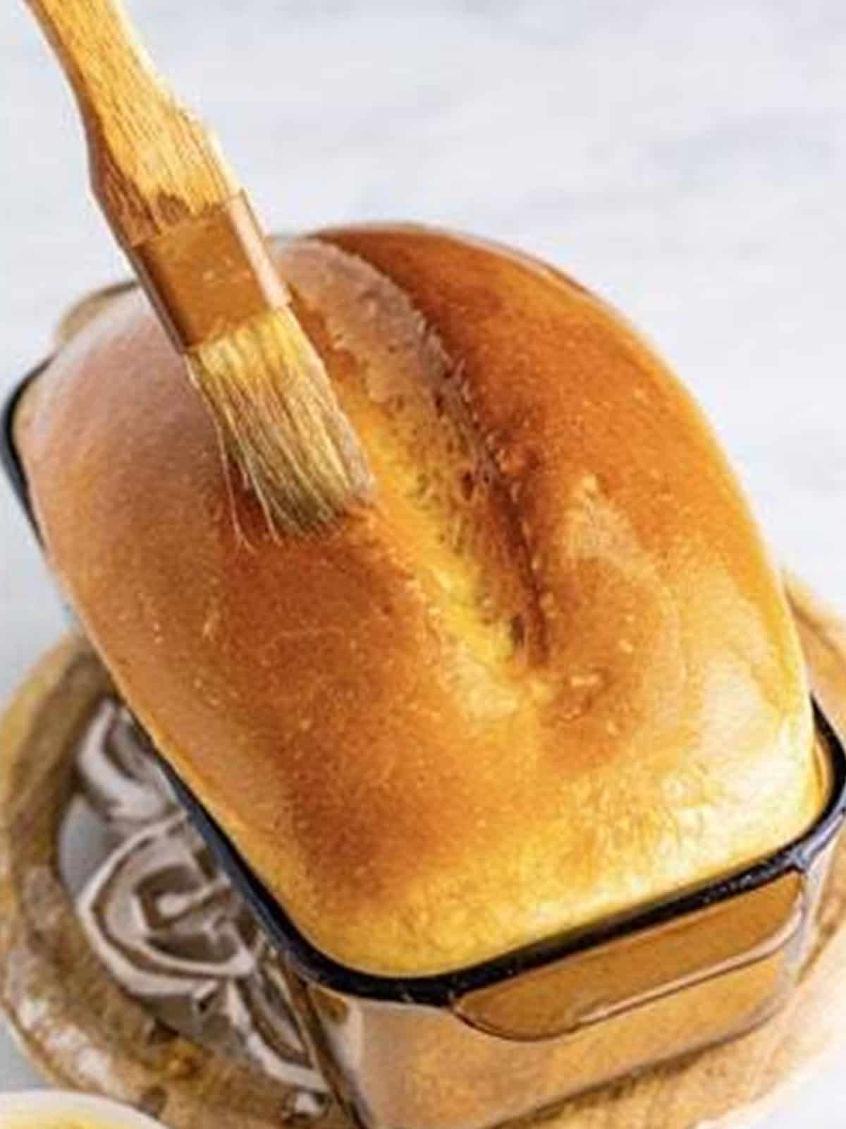 A golden baked loaf of homemade white bread brushed with butter.
