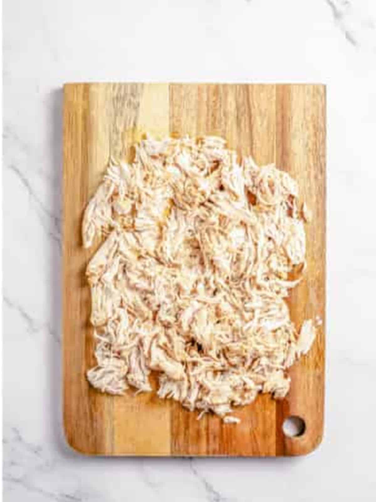 Shredded cooked chicken on a wooden cutting board for white chicken chili.
