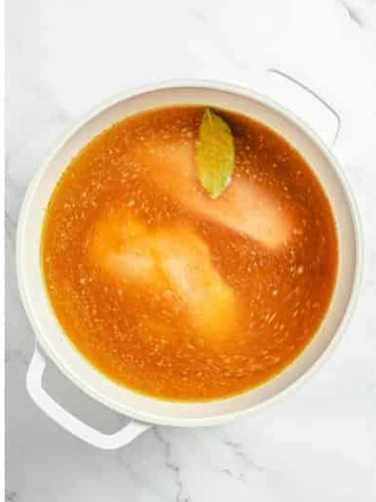 Chicken breasts simmering in seasoned broth for white chicken chili.