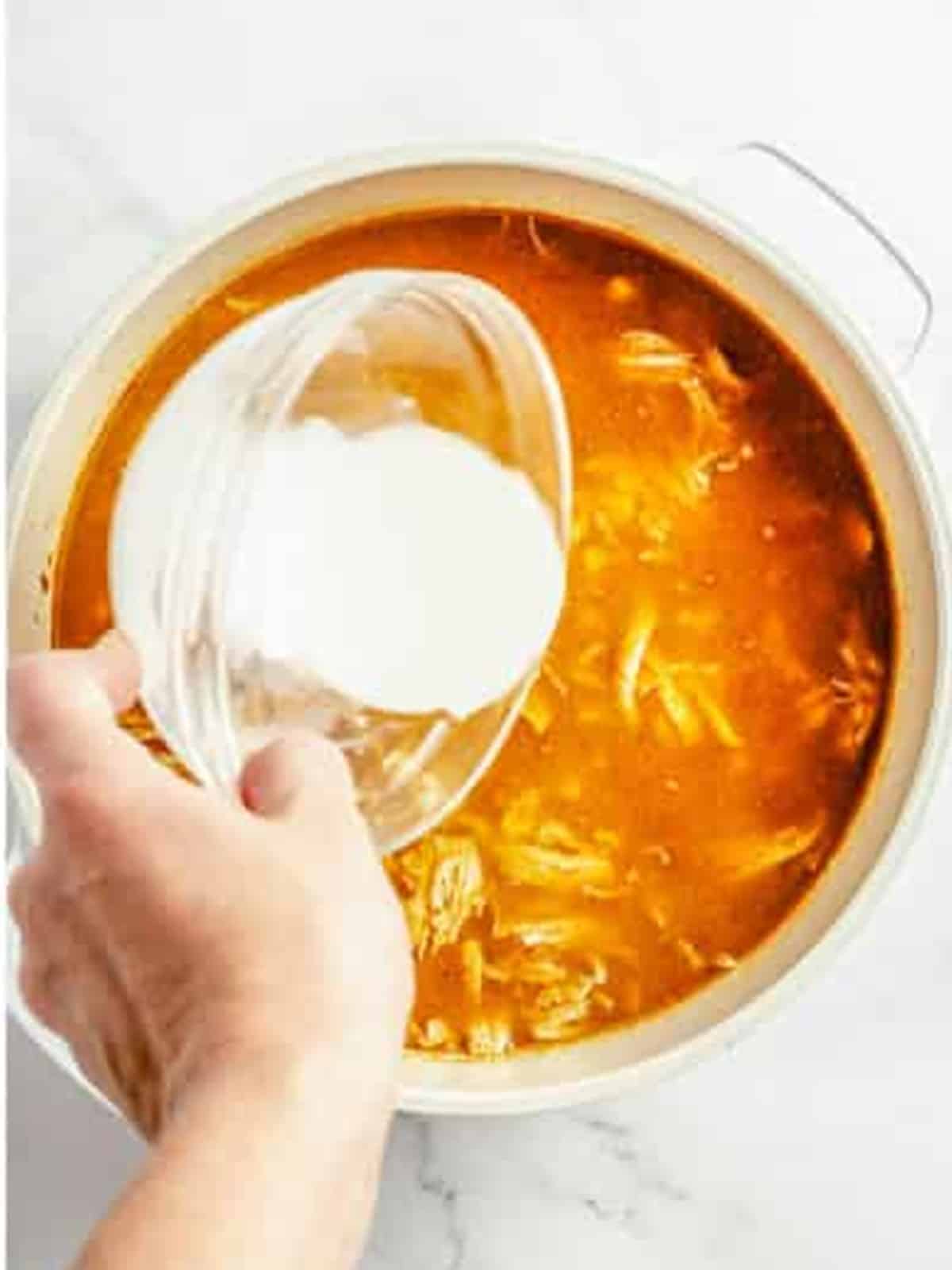 Pouring a cornstarch slurry into white chicken chili to thicken it.