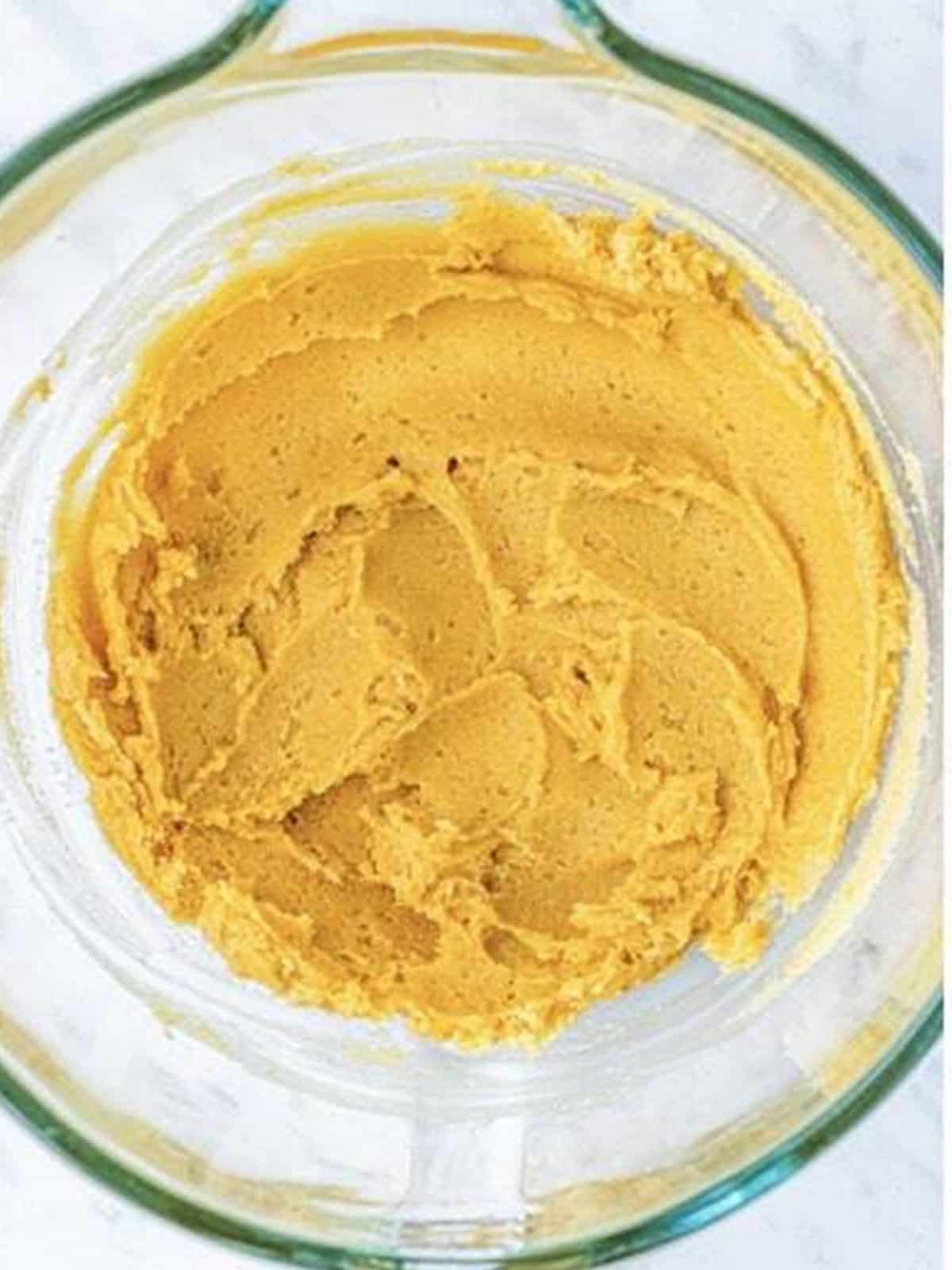 Melted butter creamed with brown and white sugar in a glass bowl for white chocolate chip cookies.