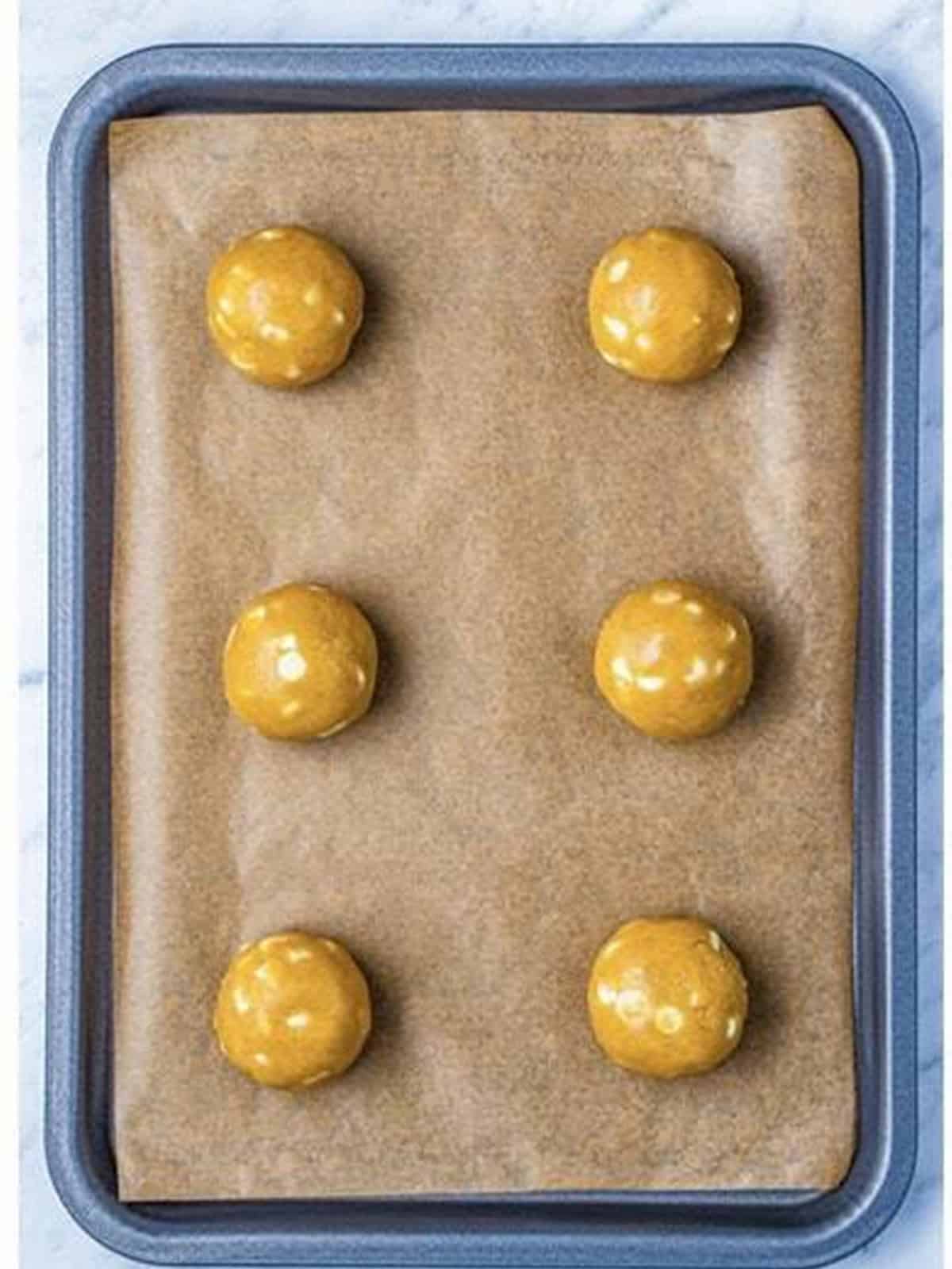 Balls of cookie dough placed on a parchment-lined baking sheet.