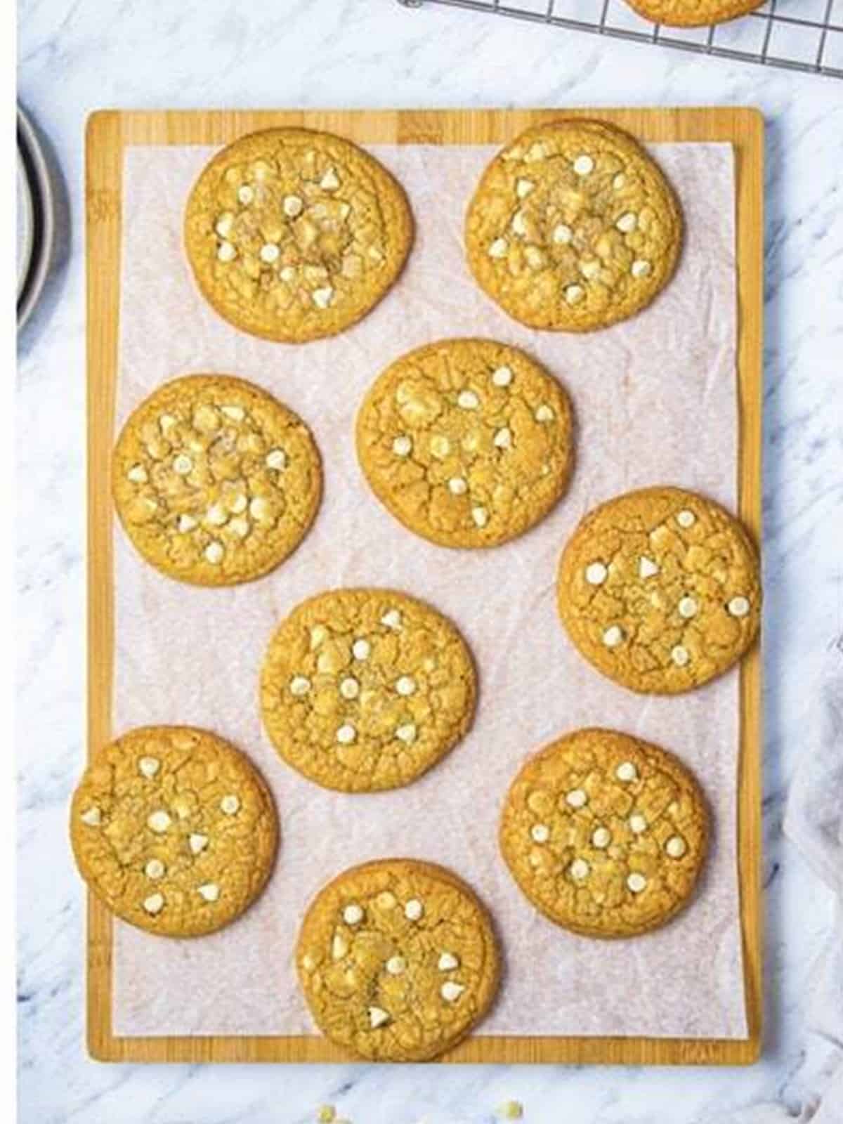Baked white chocolate chip cookies cooling on a parchment-lined tray.