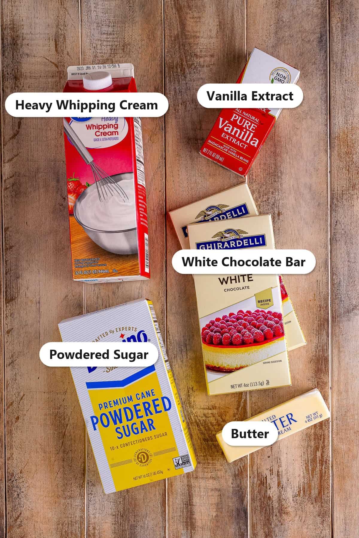 Labeled ingredients for white chocolate mousse including a white chocolate bar, heavy whipping cream, powdered sugar, vanilla, and butter.