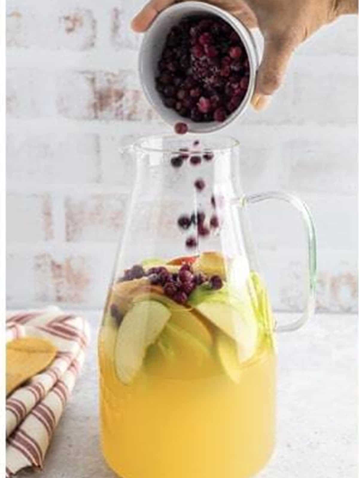 Adding cranberries to the white wine sangria pitcher.