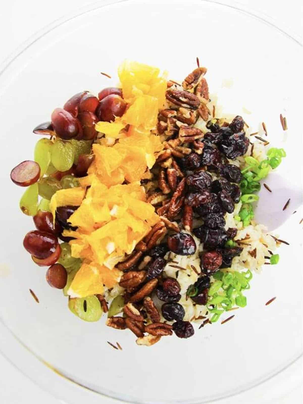 Oranges, grapes, pecans, and cranberries added to the wild rice in a bowl.