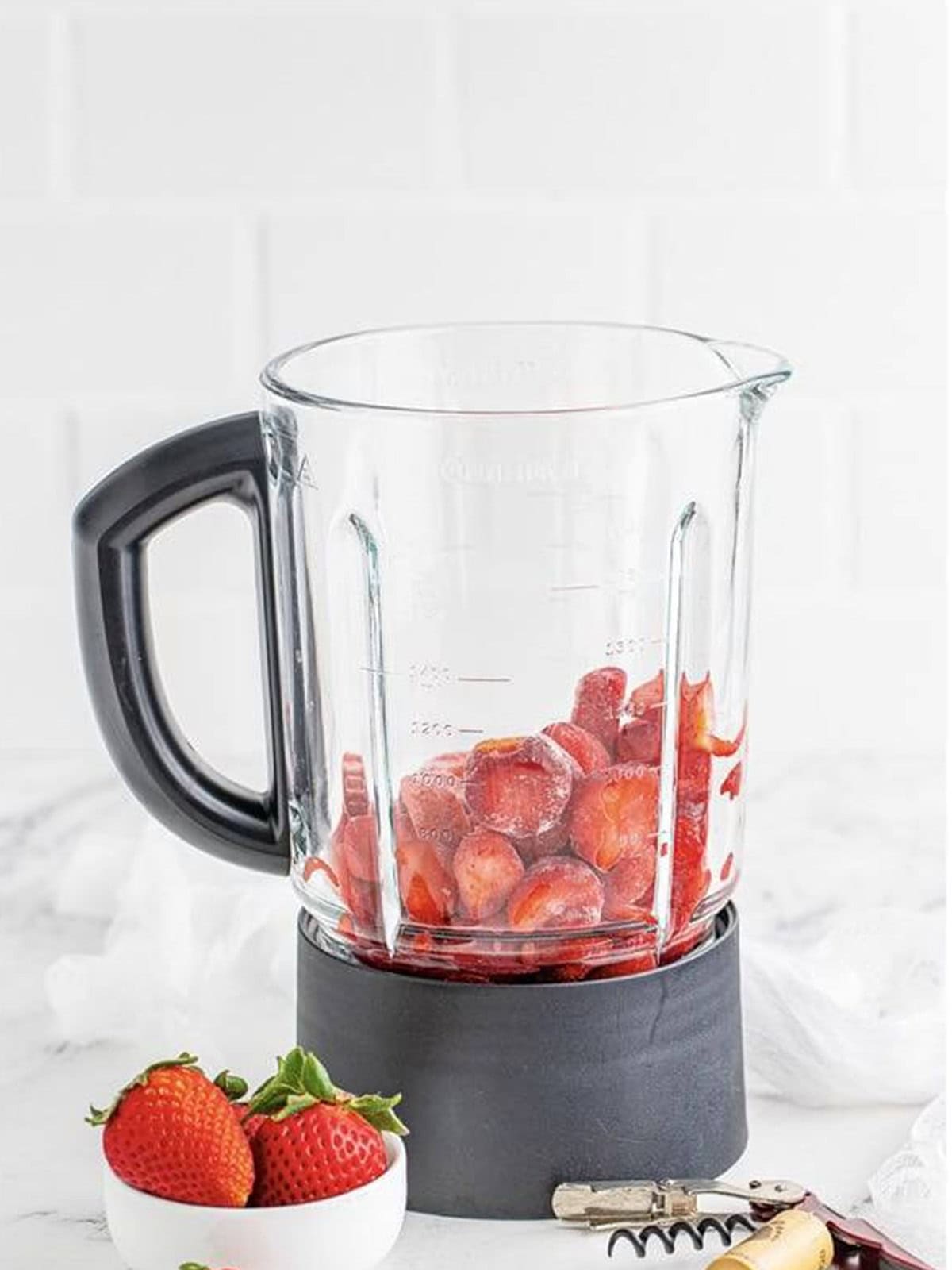 Adding frozen strawberries to a blender to make a strawberry wine slushie.