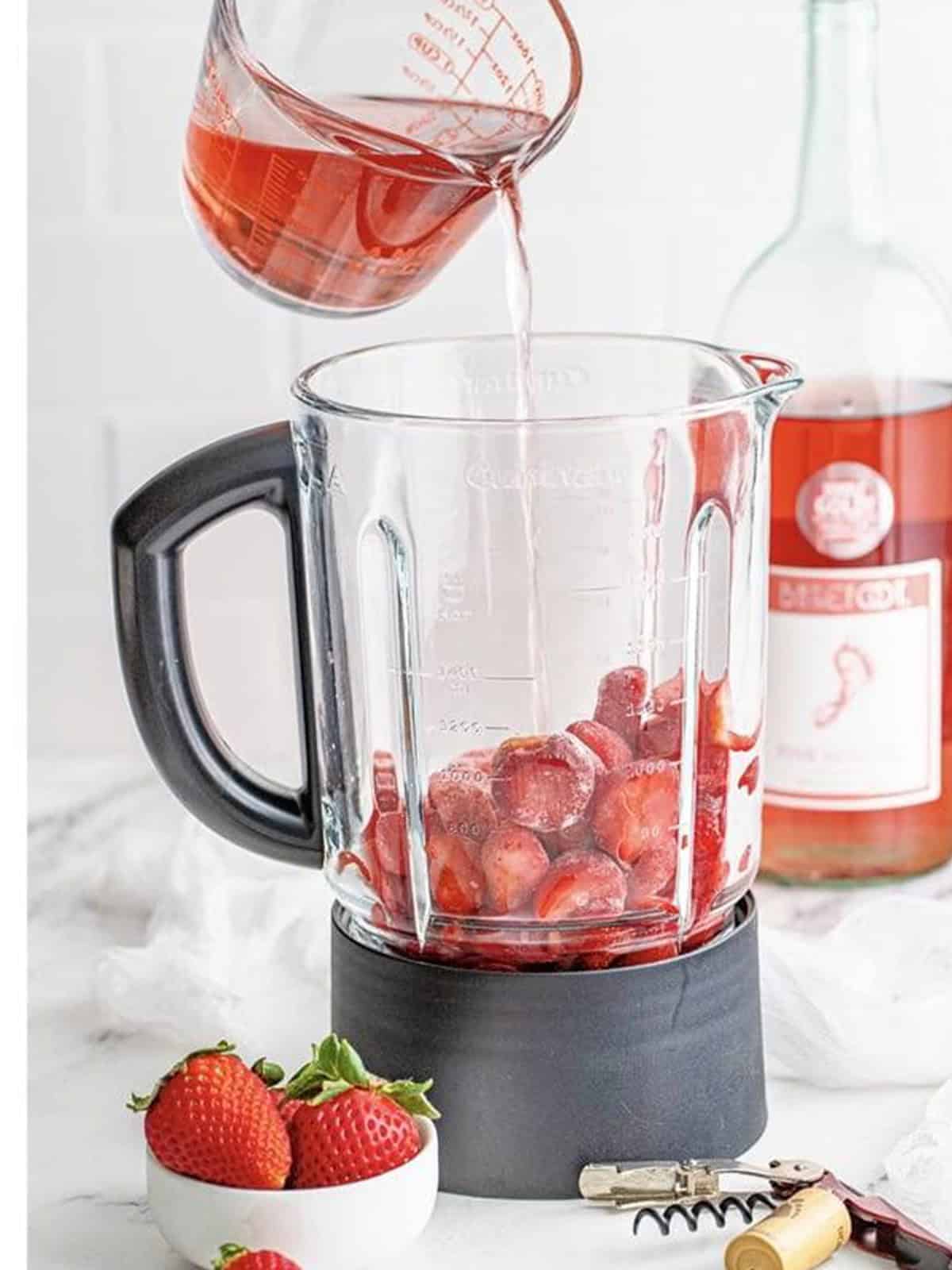 Pouring pink Moscato wine and simple syrup into the blender with frozen strawberries.