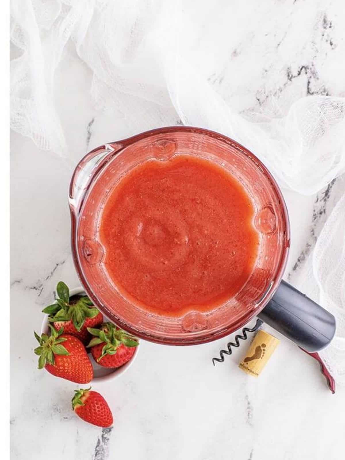 Pouring the finished strawberry wine slushie from the blender into a glass.