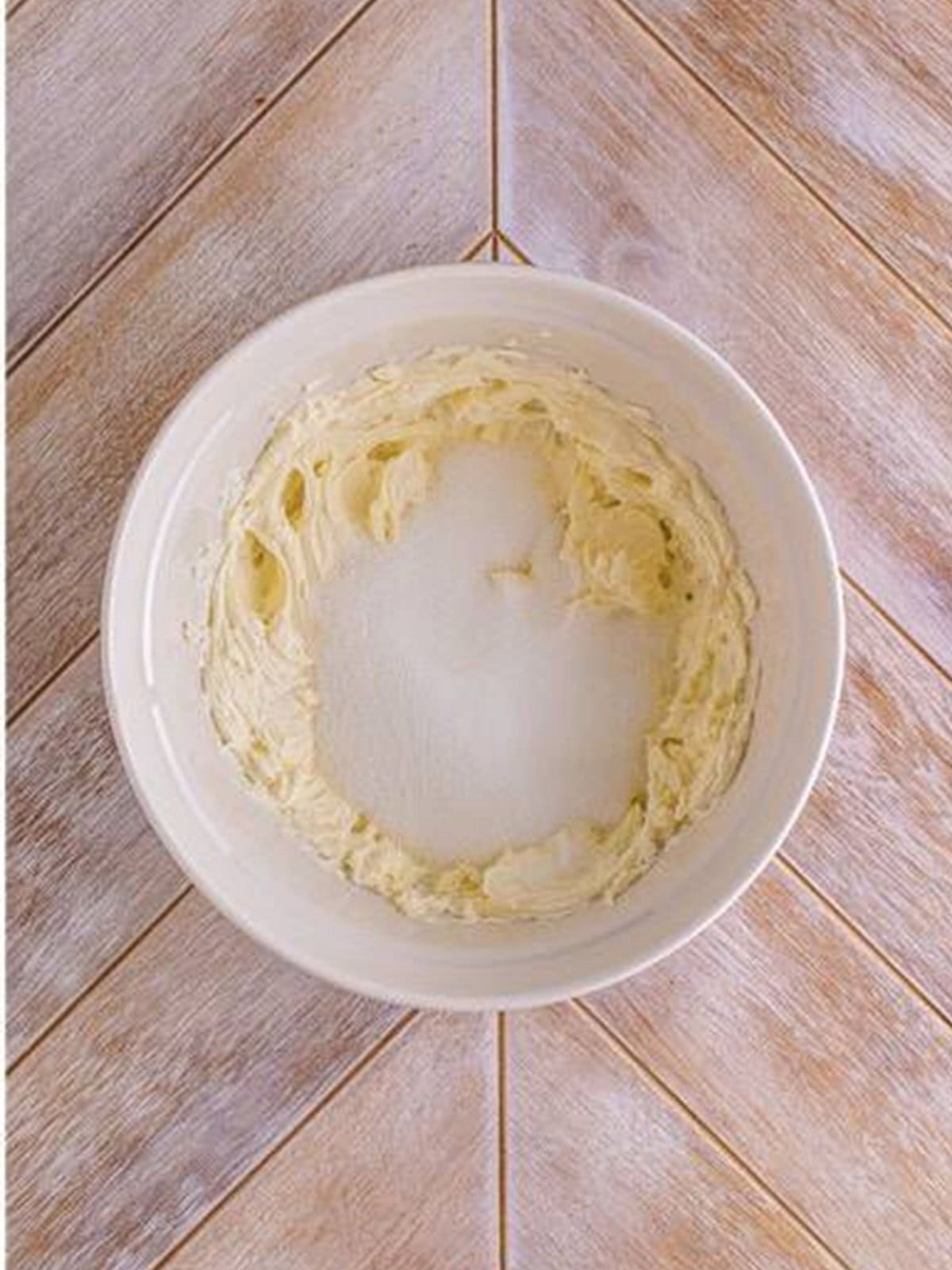 Cream cheese and sugar whipped smooth in a white mixing bowl for woolworth cheesecake recipe.