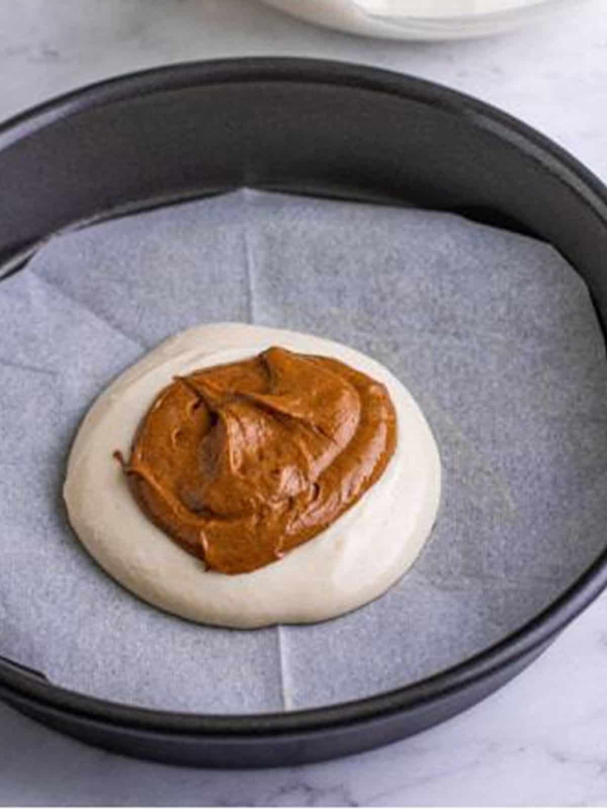 Spoonfuls of white and chocolate batter layered in the center of a cake pan to form the zebra pattern.