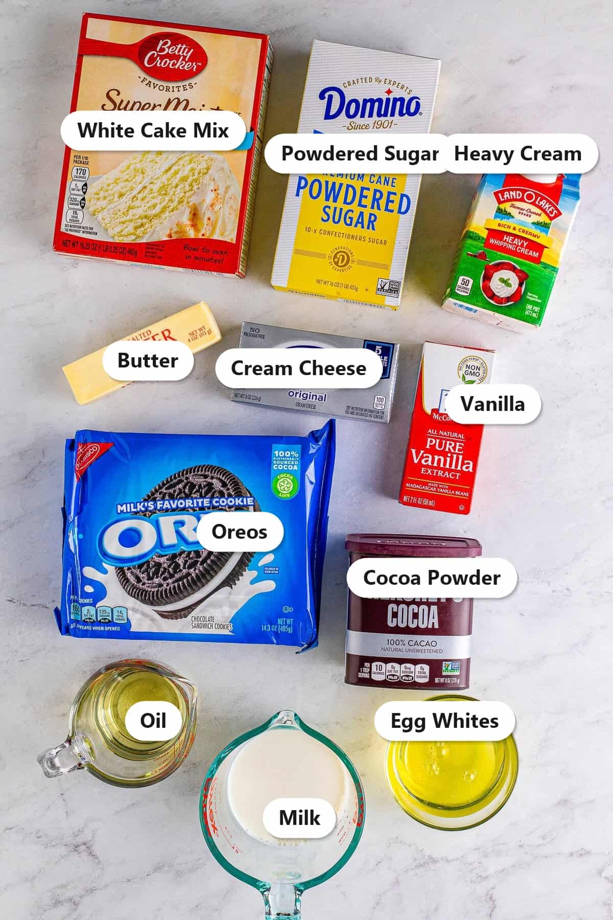 Labeled ingredients for zebra cake including white cake mix, cocoa powder, Oreos, cream cheese, butter, powdered sugar, heavy cream, vanilla, oil, milk, and egg whites.