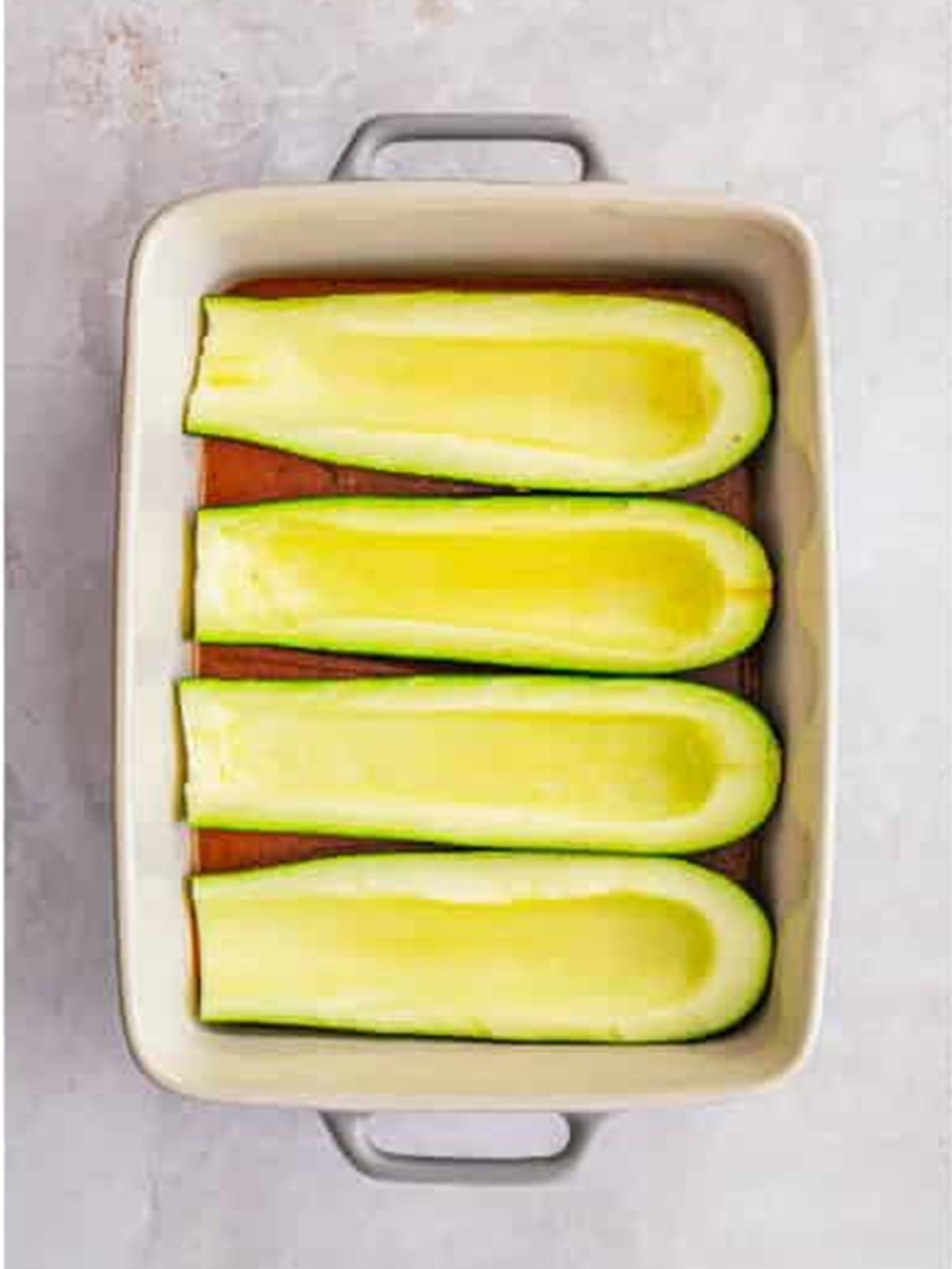 Hollowed zucchini halves arranged in a baking dish for zucchini boats.