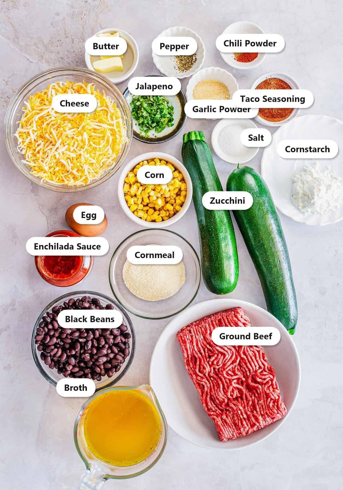 Labeled ingredients for enchilada zucchini boats including zucchini, ground beef, black beans, corn, cheese, and enchilada sauce.