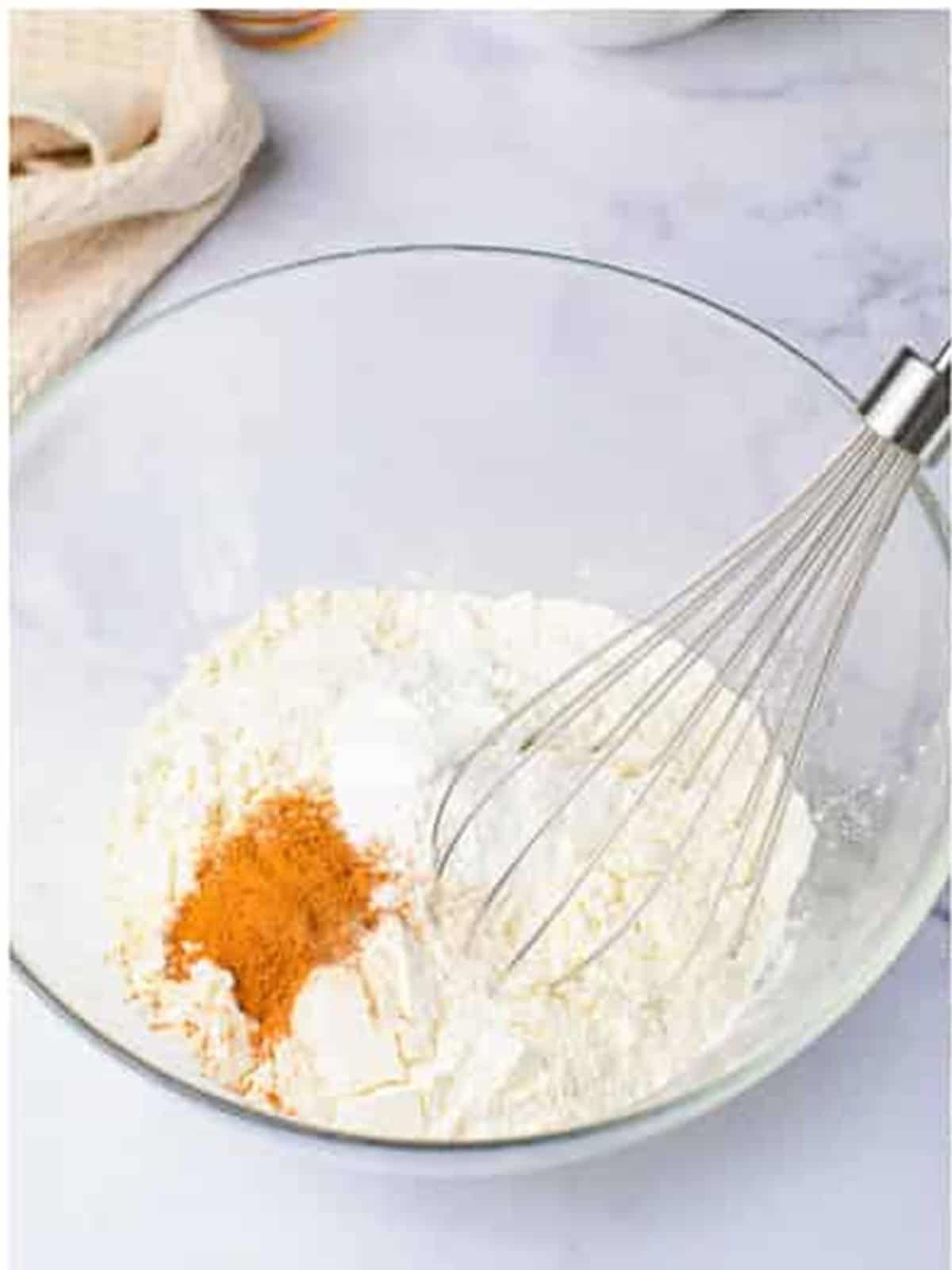 Flour, cinnamon, nutmeg, and leaveners whisked together in a glass bowl.