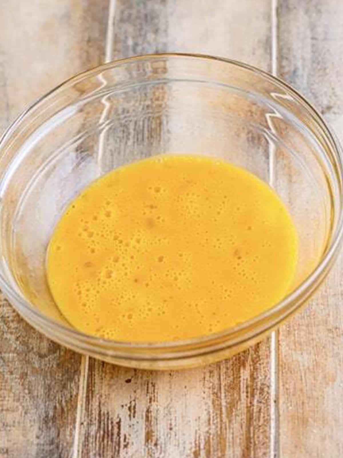 Eggs whisked with hot sauce in a glass bowl for breading zucchini.