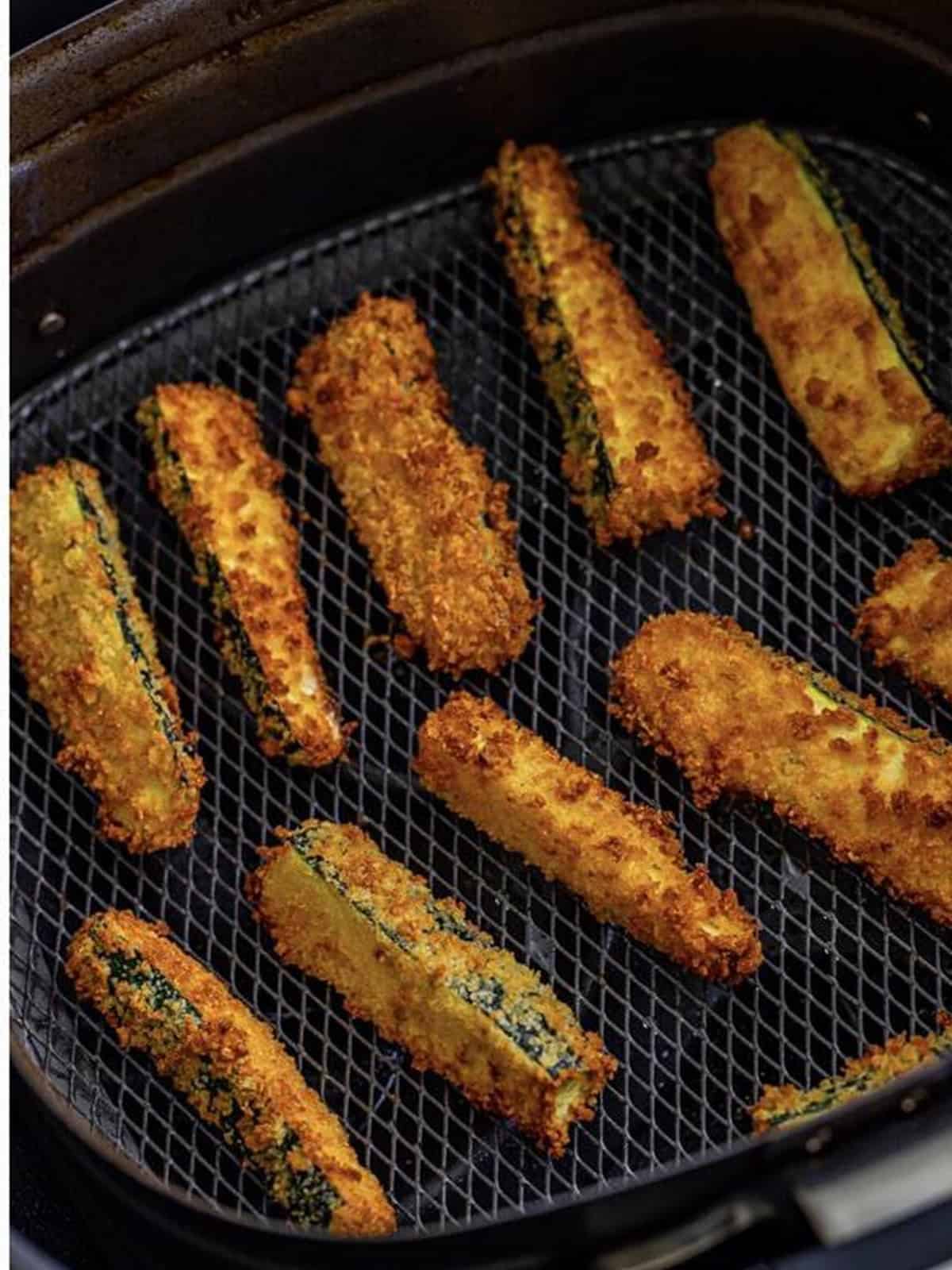 Golden crispy air fried zucchini fries in the air fryer basket.