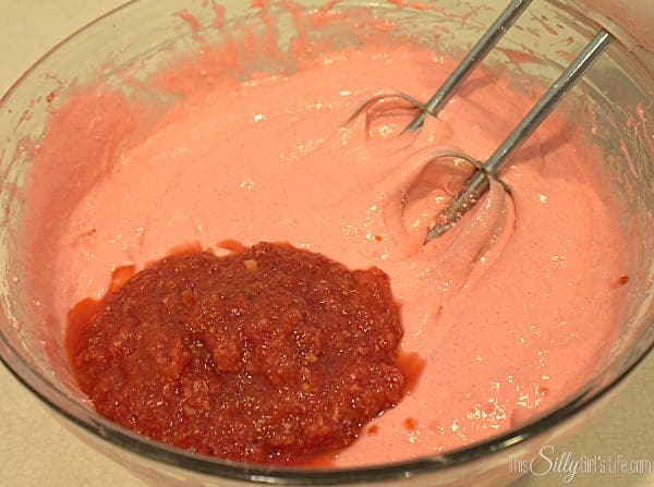 Strawberry cake batter with strawberry puree being mixed together in a glass bowl.
