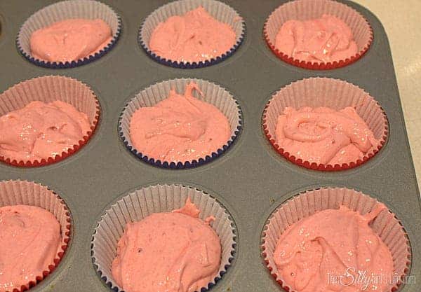 Cupcake liners filled two thirds full with pink strawberry batter in a muffin tin.