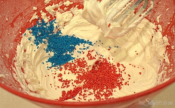 Red and blue sprinkles being folded into whipped vanilla buttercream for funfetti frosting.