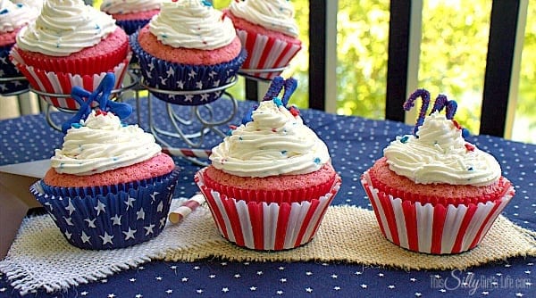 Three 4th of July cupcakes in red, white, and blue liners on a patriotic table.