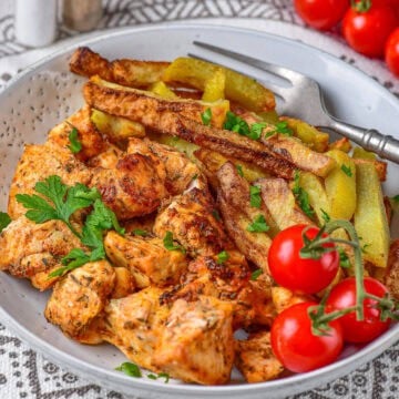 A plate of air fryer chicken and potatoes with crispy seasoned potato wedges, diced chicken, parsley, and cherry tomatoes.