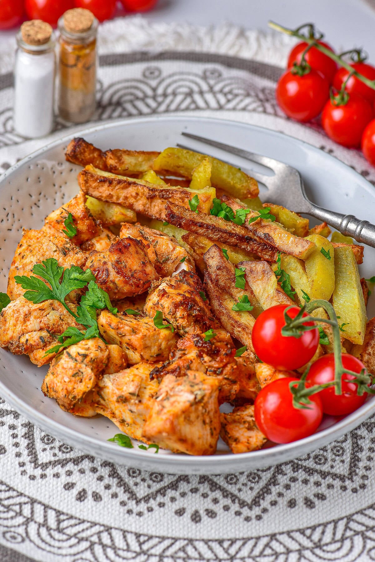 A plate of air fryer chicken and potatoes with crispy seasoned potato wedges, diced chicken, parsley, and cherry tomatoes.