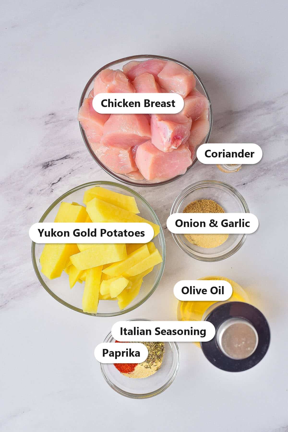 Labeled ingredients to make air fryer chicken and potatoes including chicken breast, Yukon gold potatoes, olive oil, paprika, Italian seasoning, onion, garlic, and coriander.